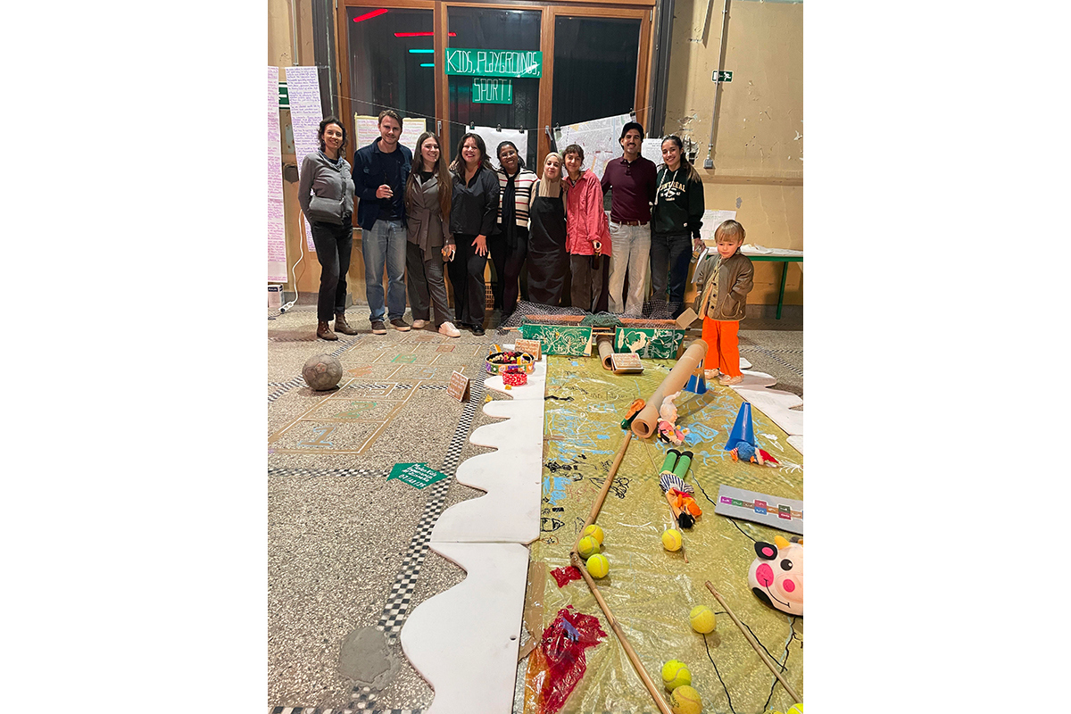 En grupp människor, framför dem ett barn som står i vad som ser ut som ett workshoparbete på golvet. Foto.