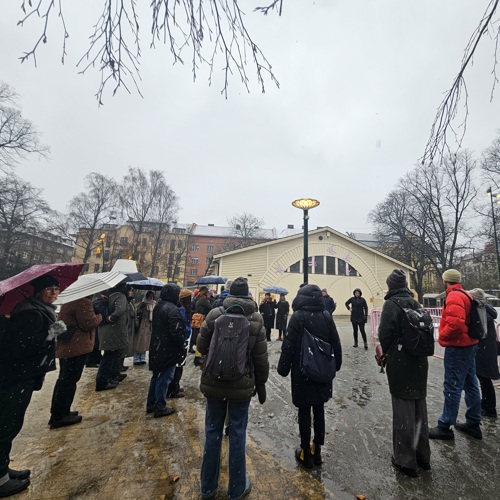 Människor i park framför äldre byggnad. Foto.