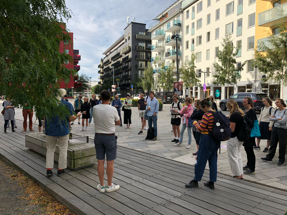 Folksamling på torg som lyssnar till guider.