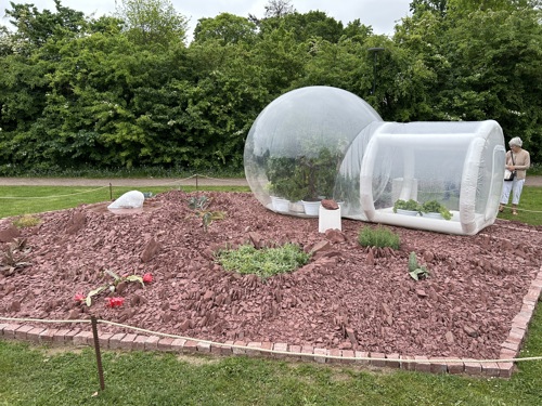 Utställningsträdgård med karg röd mark och uppblåsbart växthus. Foto.
