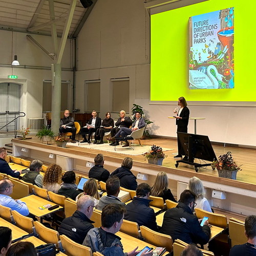 Konferenslokal med publik som ser på panelsamtal på scen. Foto.