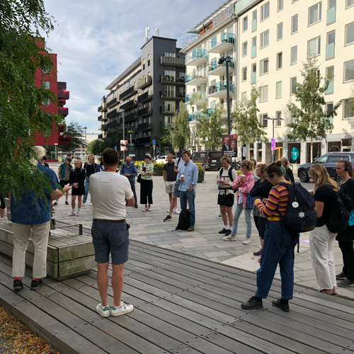 Björn och Örjan guidar grupp vid träd på torg. Foto.