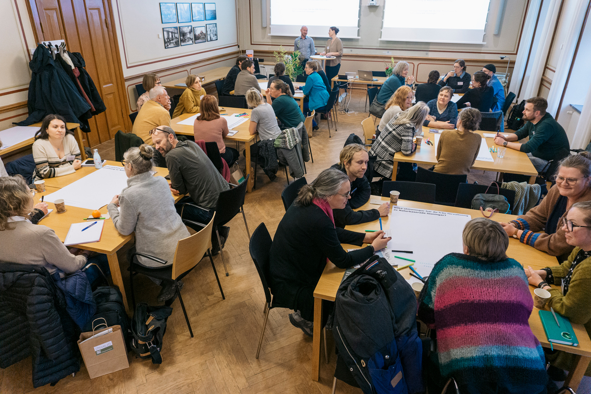 Människor sitter i grupper runt bord och diskuterar. Foto.